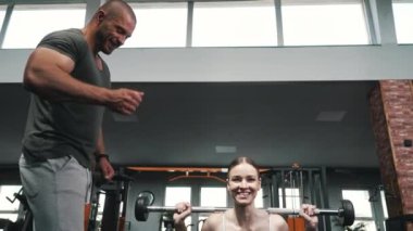 Gri spor ceketli çekici kız spor salonunda halterlerle egzersiz yapıyor. Yüksek kalite 4k görüntü