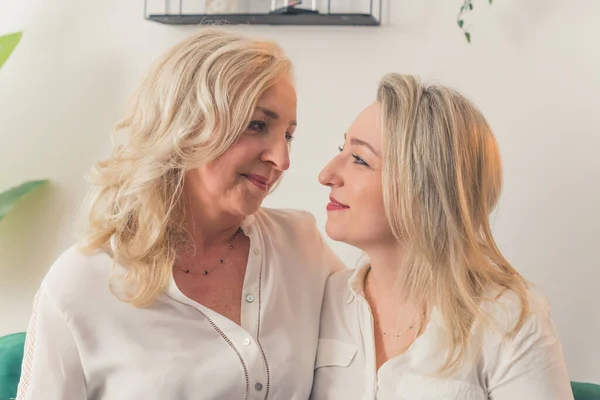 Happy elegant millenial blonde ladies sitting toghether, hugging and looking at each other with love and affection. High quality photo