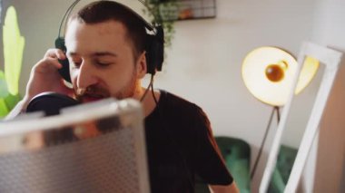 Genç erkek sanatçı evde mikrofon ve kulaklıkla müzik yaratıyor. Yüksek kalite 4k görüntü