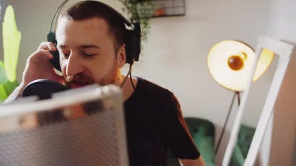 マイクとヘッドフォンのメディアを使って自宅で音楽を作る若い男性アーティスト 高品質4K映像 — ストック動画