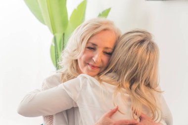 Orta yaşlı, dalgalı saçlı zarif bir bayana sarılan, düz sarı saçlı, tanınmayan beyaz bir kadın. Destek konsepti. Yüksek kalite fotoğraf