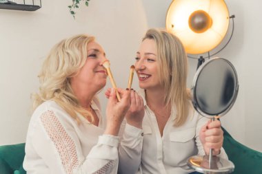 İki sarı saçlı odaklanmış çekici kadın cep aynasına bakan tüylü fırçalarla makyajlarını düzeltiyorlar. Yüksek kalite fotoğraf