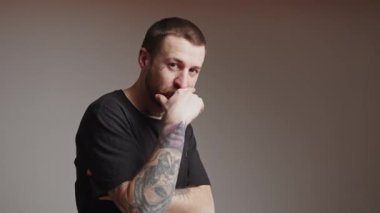 Kolunda dövmesi olan çekici beyaz adam elini ağzından tutar ve arka plandaki gri arka plan çekimini yapar. Yüksek kalite 4k görüntü