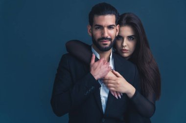 Stüdyoda, ırklar arası, zarif kıyafetler giyen, erkeğin arkasından sarılan bir kadının koyu mavi arka planı çekiliyor. Yüksek kalite fotoğraf