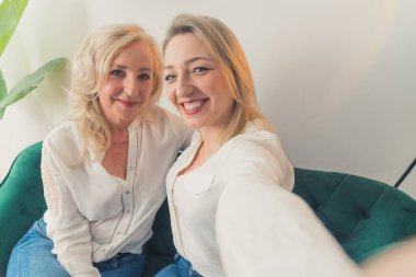 40 'larında beyaz gömlek giyen, selfie çeken, birbirine sarılan ve gülümseyen iki akraba beyaz kadın. Yüksek kalite fotoğraf