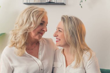 İki neşeli, beyaz saçlı, kanepede oturmuş birbirlerine bakıp gülümseyen, beyaz şık gömlekli iki kadının olduğu bir dairede çekilmiş bir fotoğraf. Yüksek kalite fotoğraf