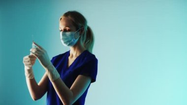 Maskeli çekici sarışın hemşire orta boy şırınga enjeksiyonu hazırlıyor. Fotokopi uzayı mavi arka plan tıbbi konsepti. Yüksek kalite 4k görüntü