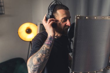 Genç dövmeli şarkıcı mikrofon ve kulaklık kullanarak müzik kaydediyor. Yüksek kalite fotoğraf