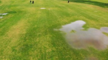 Büyük su birikintileriyle geniş yeşil bir golf sahasının insansız hava aracı görüntüsü. Bazıları golf ekipmanlarını bir sonraki deliğe taşıyor. - Evet. Yüksek kalite 4k görüntü