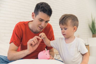 Beyaz bir baba ve oğul evdeki domuz kumbarasına para koyuyorlar. Yüksek kalite fotoğraf