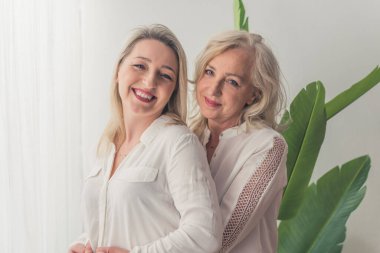 Two attractive elegant women in their 40s with blonde hair standing close to each other. One woman supporting the other one, kissing her in her cheek. High quality photo