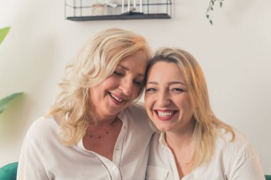 Two blonde women looking alike, wearing snow-white elegant shirts, looking directly at a camera. Females looking at each other with love and cheering. High quality photo