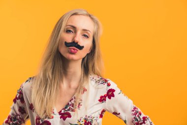 Yapay siyah bıyık takıp ördek suratı yapan komik sarışın beyaz kadın. Turuncu arka plan. Uzayı kopyala İzole stüdyo çekimi. Yüksek kalite fotoğraf