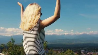 Sarışın kız, uzanmış elleriyle vadi ve dağların manzarasına bakıyor. Kovboy atışı. Yüksek kalite 4k görüntü