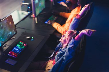 Female asian woman in her 20s pressing buttons on a lighted colorful keyboard and mouse, cheering after a phenomenal win in a video game. High quality photo