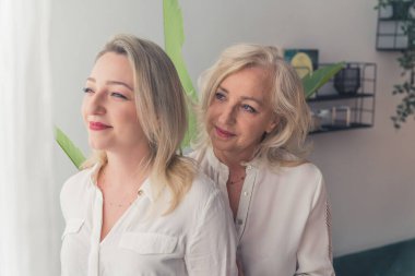 İki çekici zarif kadın, anne ve kızları birbirlerine yakın duran sarı saçlı. Bir kadın diğerini destekliyor, onu yanağından öpüyor. Yüksek kalite 4K görüntü. Yüksek kalite