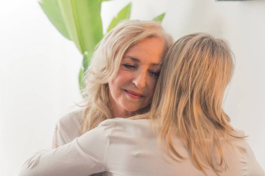 Orta yaşlı, dalgalı saçlı zarif bir bayana sarılan, düz sarı saçlı, tanınmayan beyaz bir kadın. Destek konsepti. Yüksek kalite fotoğraf