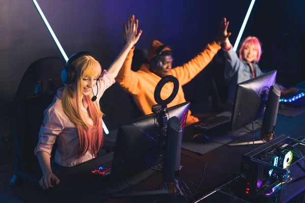 Group of young multiracial happy players sitting in gaming chairs in a professional gaming room and winning an online tournament. High quality photo