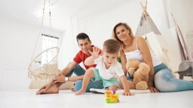 Çocuk gelişimi. Genç anaokulu çocuğu renkli oyuncaklarıyla oynarken ailesi ona tezahürat yapıyor. Modern beyaz oturma odası. - Evet. Yüksek kalite 4k görüntü