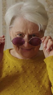 Güzel, yaşlı, beyaz bir kadın ev ortamında güneş gözlüğü takıyor. Son sınıf öğrencileri kavramına yakın çekim yapıyor. Yüksek kalite 4k görüntü