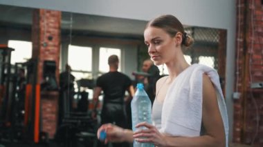 Kafkasyalı, gülümseyen ve su şişesini kapatan genç bir kadının kapalı spor salonu portresi. Refah kavramı. Yüksek kalite 4k görüntü