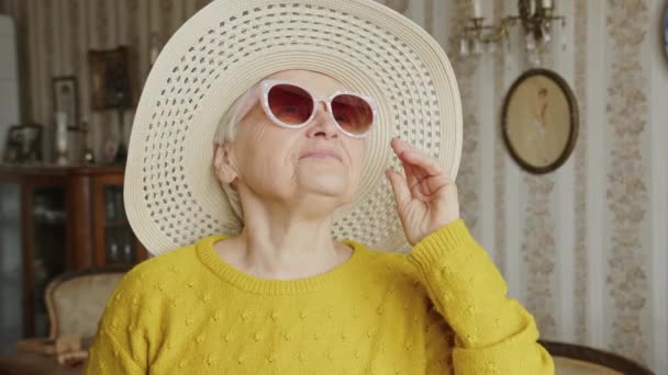 ピンクのサングラスとハットの笑顔を持つ遊び心とかなりシニア白人女性幸せな中アップ室内年功序列の概念 高品質4K映像 — ストック動画