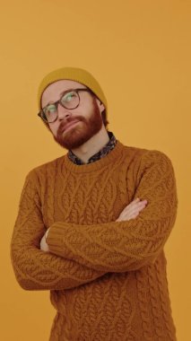 Thoughtful bearded Hipster in his 30s wearing the sweater and winter hat thinking - orange background Vertical. High quality 4k footage