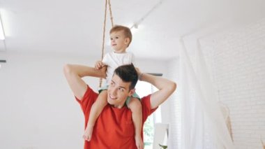 Mutlu bir baba, oturma odasında boynunu taşıyan küçük oğlunu taşıyor. Babalık kavramı. Yüksek kalite 4k görüntü