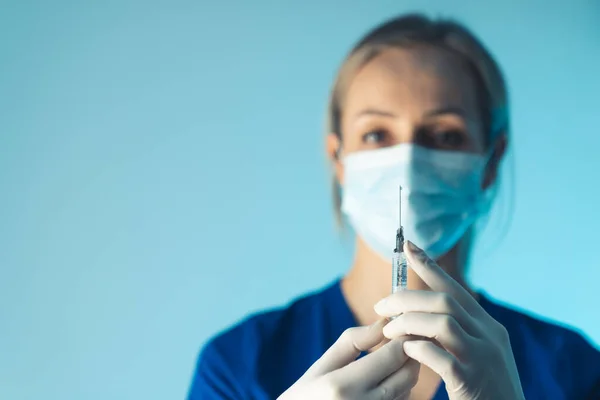 nurse with a protective mask holiding a vaccination syringe - light blue background closeup. High quality photo