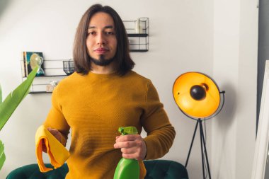 Sakallı, siyah saçlı bir adam yeşil el spreyi ve elinde bir bez tutuyor. Yüksek kalite fotoğraf