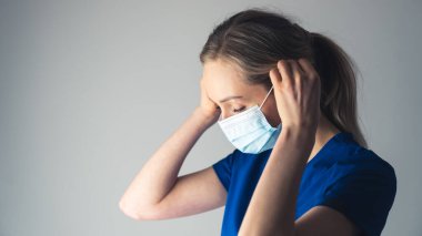 young female nurse putting on a protective mask - light blue background closeup. High quality photo