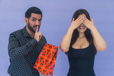 Hediye sürprizi. Sevgililer günü, doğum günü, yıldönümü konsepti. Resmi gömlekli yakışıklı Kübalı adam, yanında duran ve gözlerini kapatan kız arkadaşına kırmızı kağıt bir hediye paketi veriyor. Yüksek