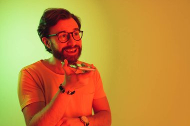 Stüdyo ortamında renkli ışıklarla akıllı telefondan konuşan sakallı şık bir genç adam. Yüksek kalite fotoğraf