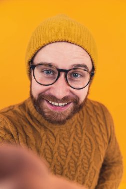Selfie makineli gülümseyen genç adam, beyaz sakallı hippi elinde akıllı bir telefon, video görüşmesiyle konuşuyor, turuncu arka plan. Yüksek kalite fotoğraf