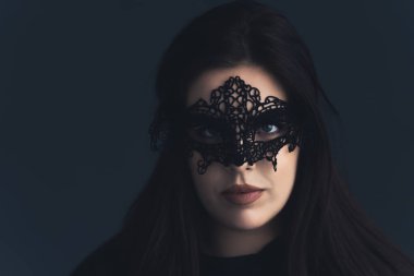 Siyah arka planda siyah gözlü, dantel maskeli bir kadın kameraya bakıyor..