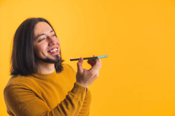 A happy long haired person on a yellow and orange background talking to a mobile phone listening in a room. High quality photo