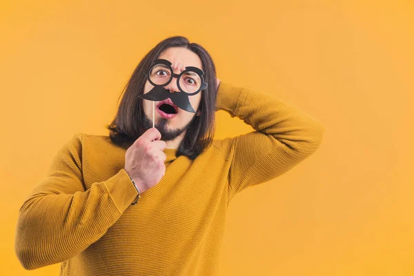 A shocked male person holding a moustache and grabbing his head in a studio on a yellow background. High quality photo