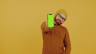 Genç adam yeşil krom anahtarlı akıllı telefon ekranını gösteriyor ve başparmağını kaldırıyor. Yüksek kalite 4k görüntü