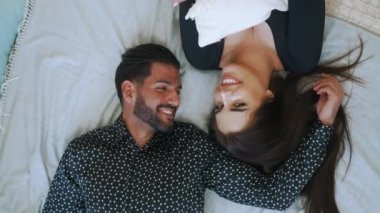 Love between two people. Happy heterosexual married couple lying on bed, looking each other in the eye in a romantic way, and smiling. High quality 4k footage