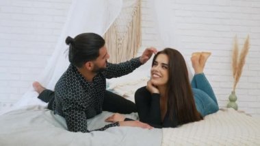 Cute couple looking at each other while layong on the bed, smiling broadly and enjoying time together. High quality 4k footage