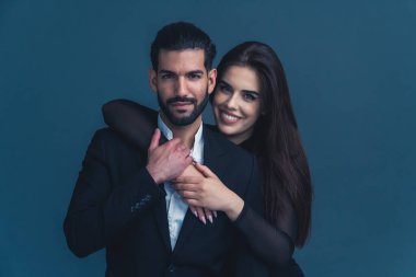 Siyah takım elbiseli yakışıklı Kübalı sakallı adam kameraya bakıyor ve uzun saçlı, geniş gülüşlü güzel beyaz bir kız tarafından arkadan tutuluyor. Stüdyo izole edildi. Yüksek kalite