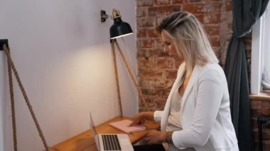 Genç, beyaz, hamile bir kadın elinde bir not defteri ve dizüstü bilgisayarla çalışıyor. Orta boy, uzaktan kumandalı ev işi konsepti. Yüksek kalite 4k görüntü