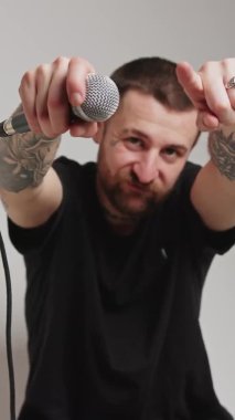 Vertical video - Attractive Caucasian man moves hands, microphone in hands, pointing to the camera grey background isolated medium shot studio shot. High quality 4k footage