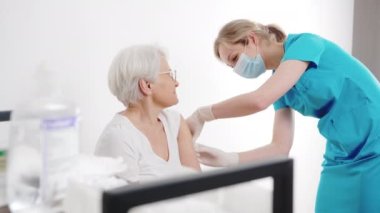 Genç bir hemşire hastanedeki yaşlı, gri saçlı bir kadına ilaç ya da anti-covid aşısı yapıyor. Yüksek kalite 4k görüntü