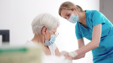 Tıp kliniğinde kıdemli bir kadın hastaya yüz maskesi takan bir hemşire. Yüksek kalite 4k görüntü