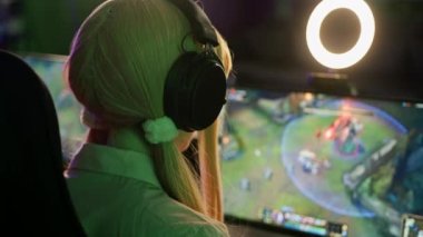 Unrecognisable teenage girl wearing headphones playing an online game on wide screen with ring light. Gaming computer setup. . High quality 4k footage