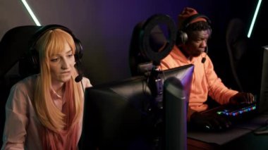 Teenage white girl wearing headset smiling competing in online game tournament with her friend. Blue lighting. High quality 4k footage