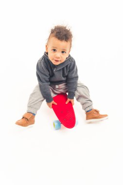 Beş yaşında Afro-Amerikan bir çocuk kaykayın üzerinde oturuyor ve kameraya bakıyor. Beyaz arka plan. Yüksek kalite fotoğraf