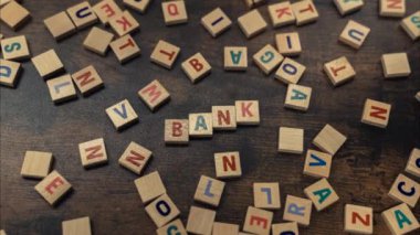 BANK. Money and savings concept. Scattered colourful wooden letter puzzles creating the word bank. Wooden table as a background. Top view. High quality 4k footage