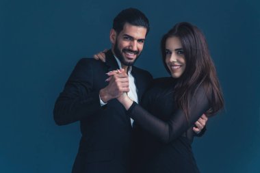 Siyah elbiseli, siyah saçlı kadınla dans eden, takım elbiseli İspanyol bir adam. Genç bir çift. Karanlık arka plan stüdyo çekimi. Yüksek kalite fotoğraf